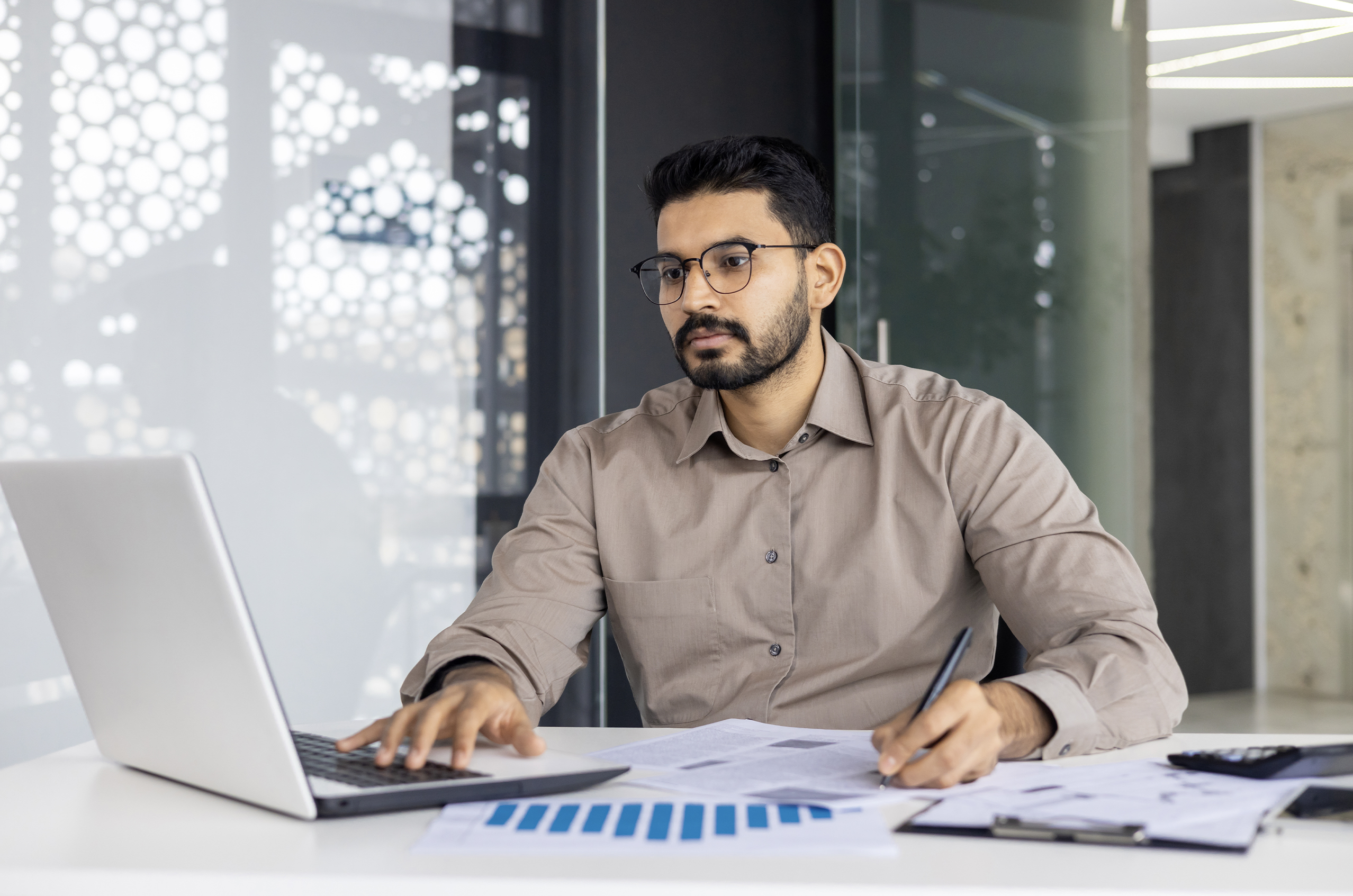 Man in glasses working on a laptop at a modern office desk.
